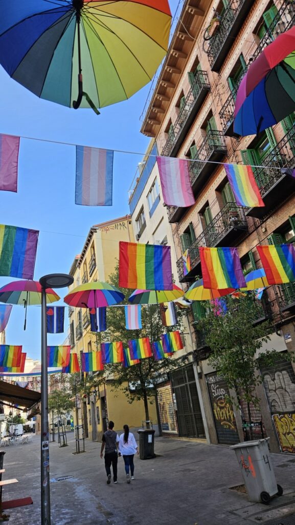 Decorated bar area in Chueca during Madrid Pride, with rainbow flags and festive street decorations.