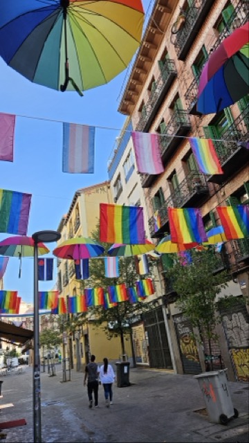 Decorated bar area in Chueca during Madrid Pride, with rainbow flags and festive street decorations.