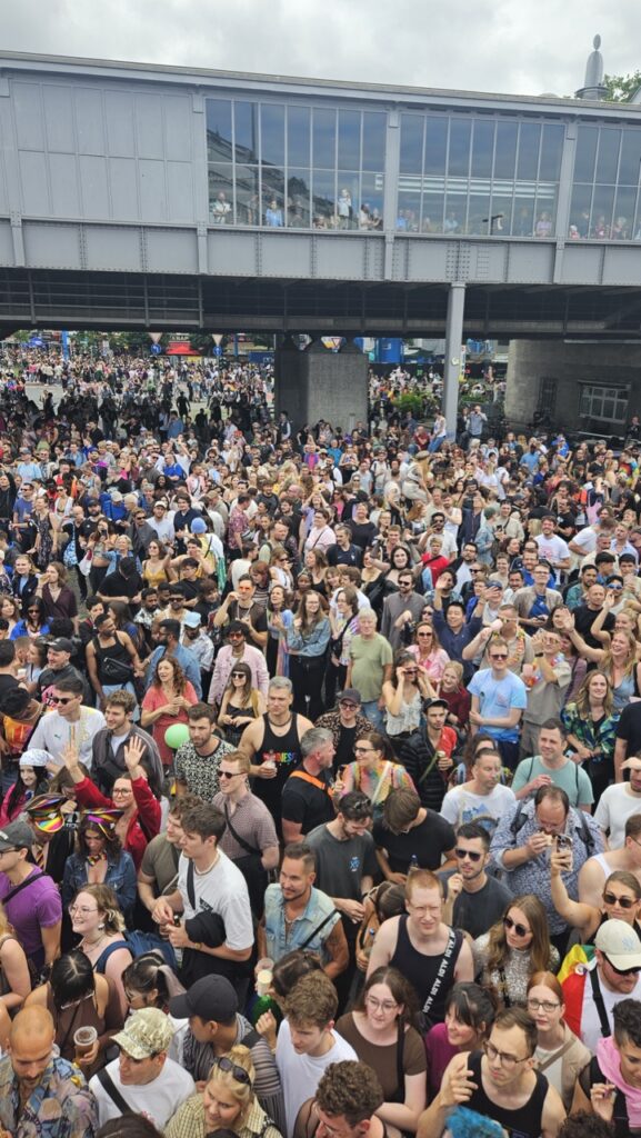 Crowds celebrating Berlin Pride at Nollendorfplatz with the historic U-Bahn viaduct visible above the street