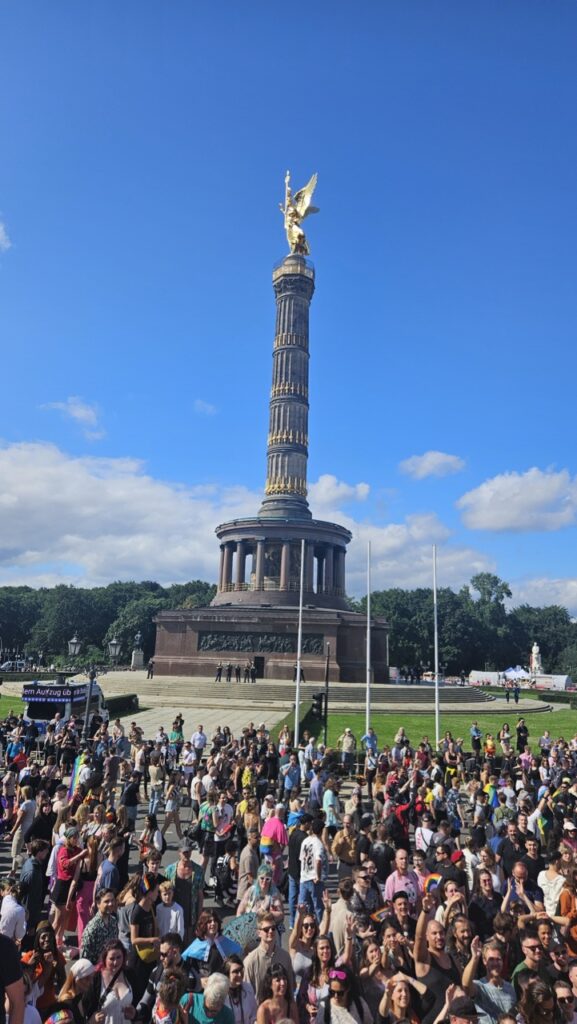 Berlin Pride parade crowds and floats with the Siegessäule (Victory Column) visible in the background during CSD Berlin