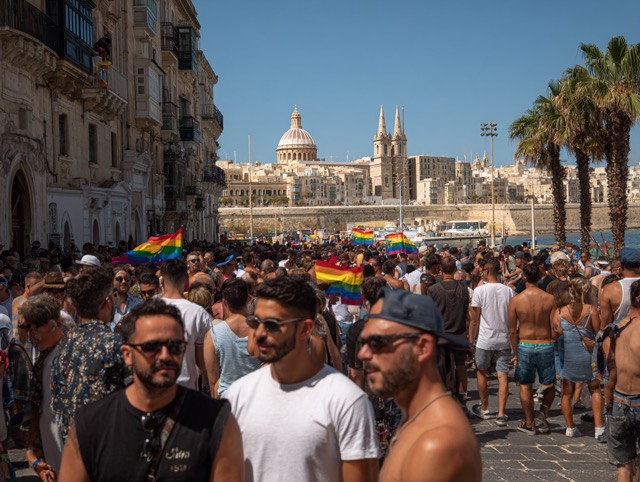 A large group of men holding rainbow flags at the Malta Pride parade.
