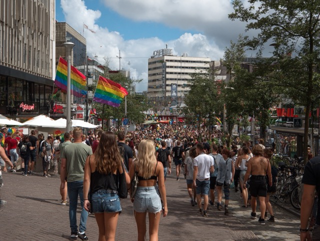 A crowd of people holding rainbow flags at a Pride event in Rotterdam.