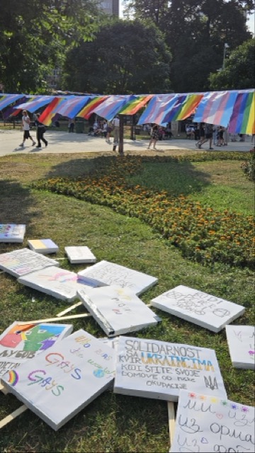 Political signs and boards with messages about LGBT rights and equality on a grass field in a park during Pride.