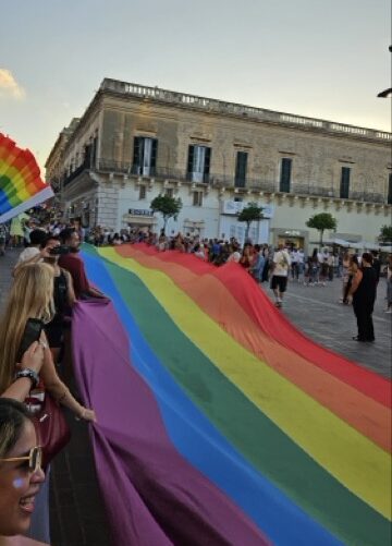 A massive rainbow flag is carried by a group of participants through the historic city center during Malta Pride.