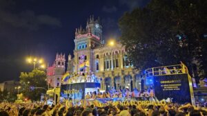 Colorful floats and crowds celebrating Madrid Pride parade at night, with rainbow lights and people dancing through the city streets.