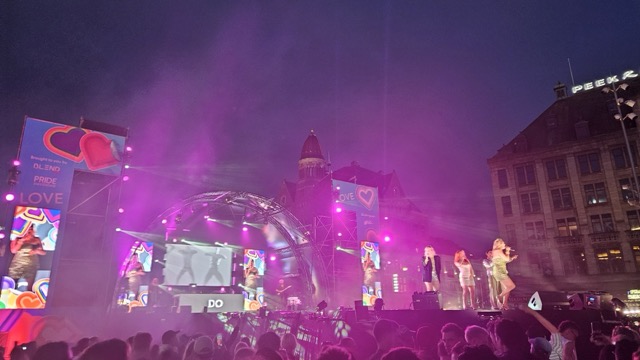 Crowd celebrating at Amsterdam Pride concert on Dam Square, people enjoying live music on the main stage.