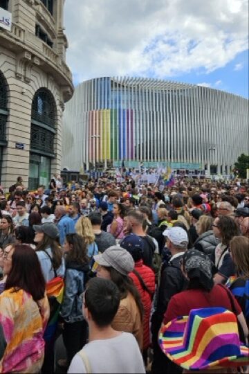 People marching through the Brussels city centre during Brussels Pride, waving rainbow flags and celebrating LGBTQ+ pride in the streets.