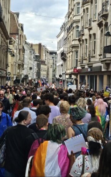 People marching through the Brussels city centre during Brussels Pride, carrying rainbow flags and celebrating LGBTQ+ pride in the streets.