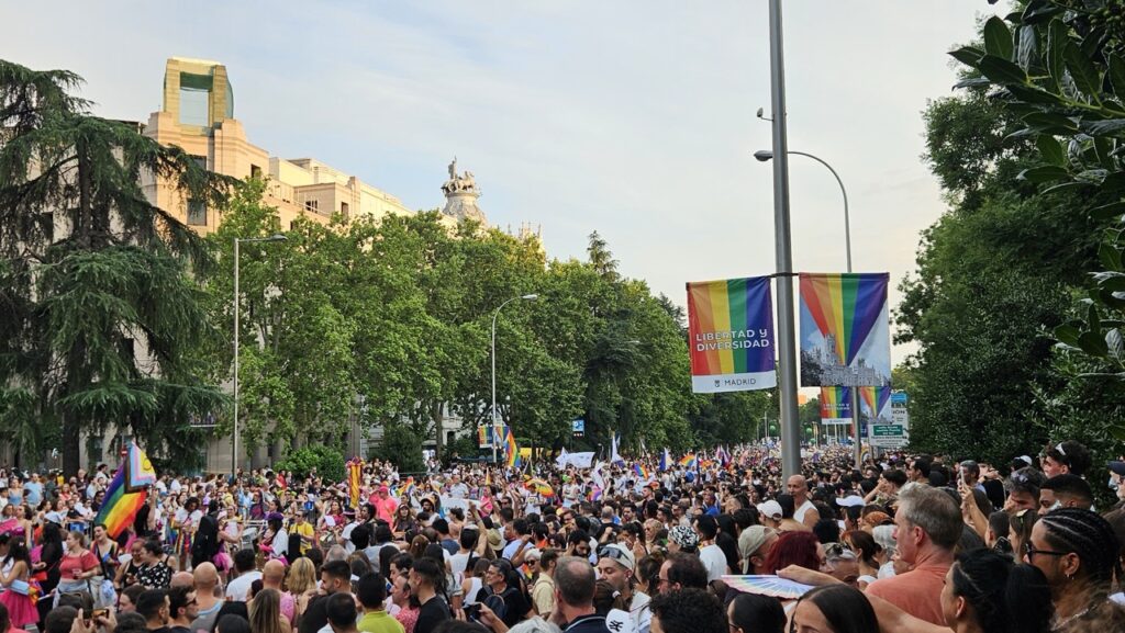 Large crowd celebrating during the Madrid Pride parade, with people waving rainbow flags and filling the streets.