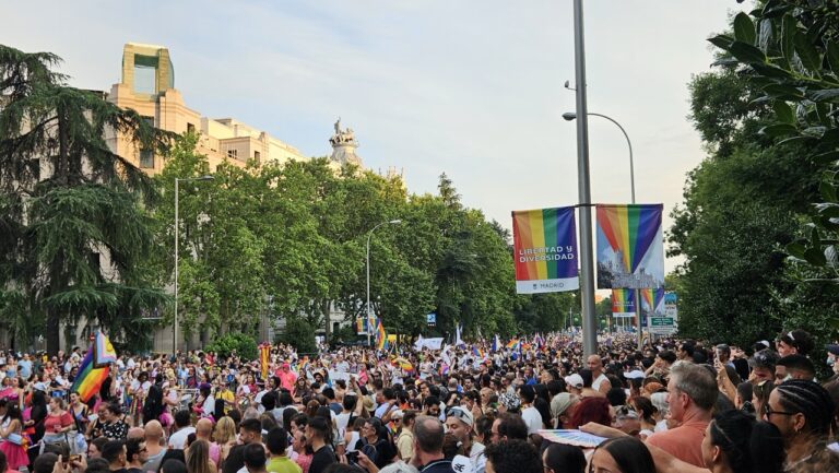 Large crowd celebrating during the Madrid Pride parade, with people waving rainbow flags and filling the streets.