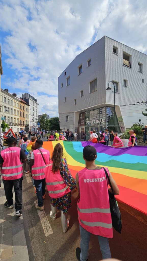 Front of the Brussels Pride march in the city centre, with a large rainbow flag carried by many participants celebrating LGBTQ+ pride.