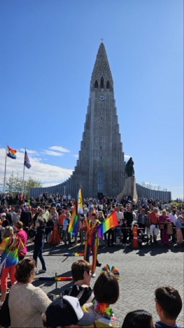 People marching during Reykjavík Pride with rainbow flags, passing through the city streets with a church visible in the background.