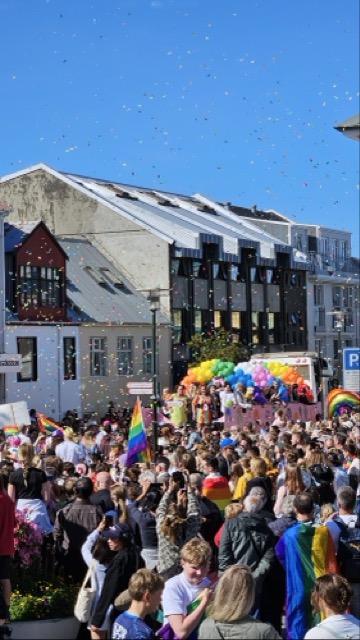 People marching during Reykjavík Pride with rainbow flags, with a decorated float in the background.