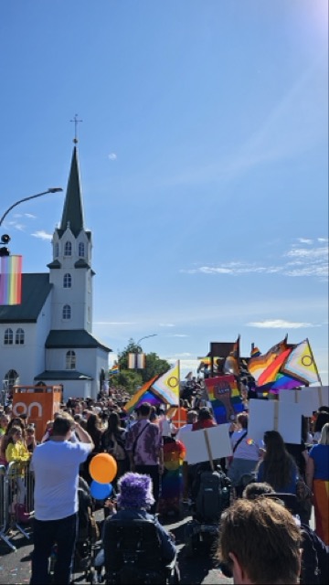 People marching during Reykjavík Pride with rainbow flags, passing through the city streets.