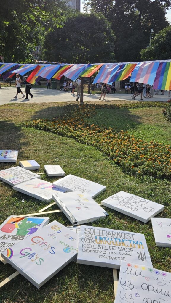 Political signs and boards with messages about LGBT rights and equality on a grass field in a park during Pride.