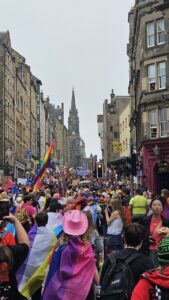 People marching through the streets during Edinburgh Pride, having rainbow flags and celebrating LGBTQ+ pride in the city centre.