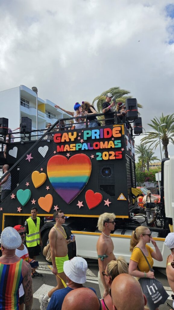 Crowd celebrating Maspalomas Pride in Gran Canaria, waving rainbow flags and enjoying the outdoor pride festival atmosphere.