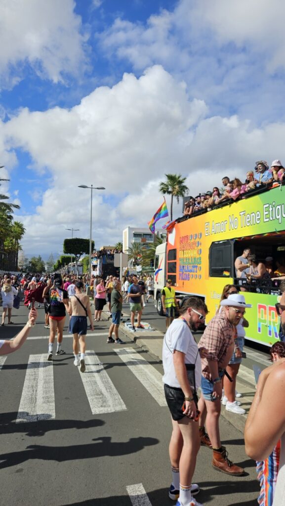 Colorful Pride floats and crowds celebrating during Maspalomas Pride in Gran Canaria, with rainbow flags and festive decorations.