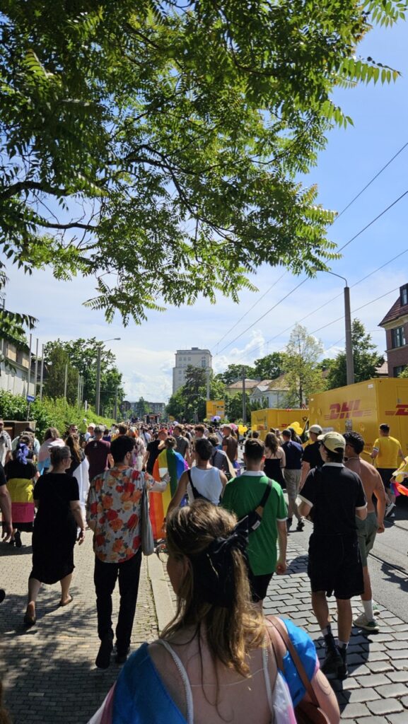 Crowd marching through Dresden city centre during Dresden Pride, with people celebrating LGBTQ+ pride and waving rainbow flags.