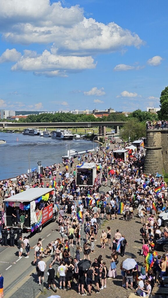 People gathering near the Elbe River at the end of the Dresden Pride parade, celebrating LGBTQ+ pride in the city.