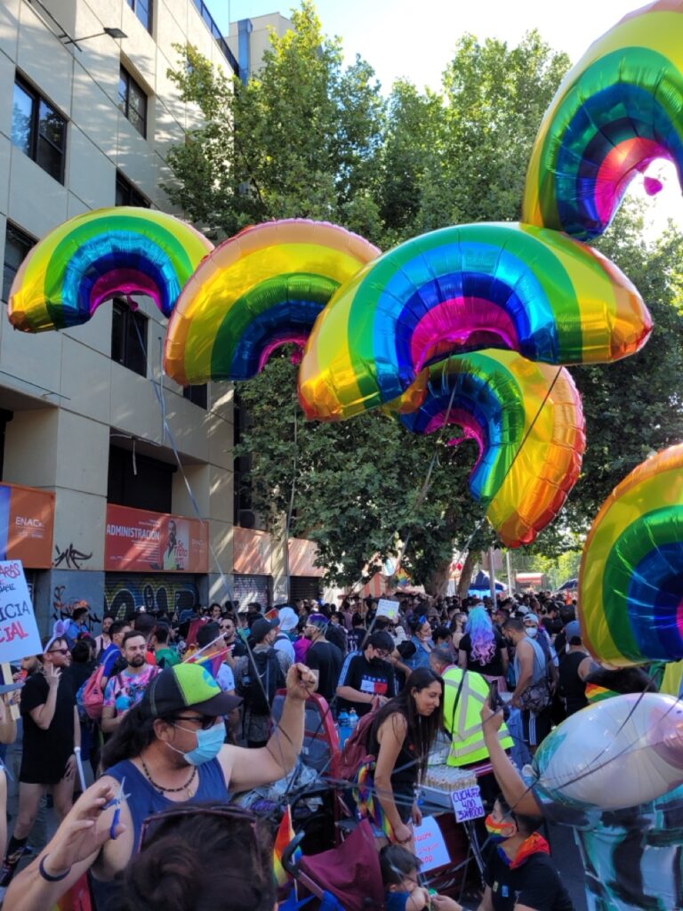 Crowd celebrating during a Pride parade in South America, with people waving rainbow flags and enjoying LGBTQ+ festivities.