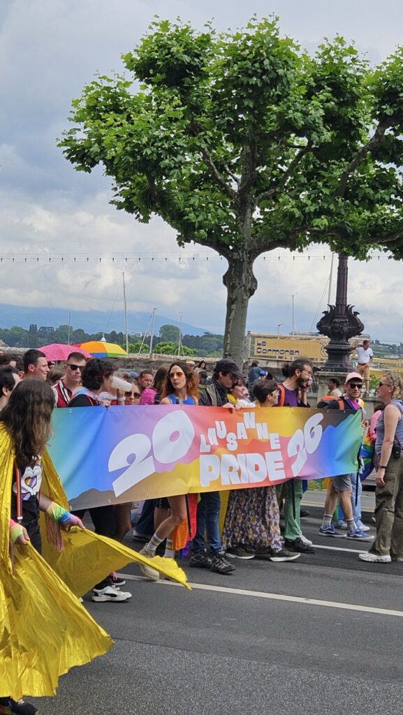 Front of the Geneva Pride parade with participants carrying a banner promoting the next Western Switzerland Pride in Lausanne.