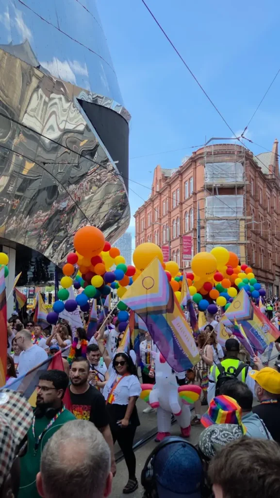Participants march through Birmingham city centre during Birmingham Pride, carrying rainbow flags and banners along the parade route.