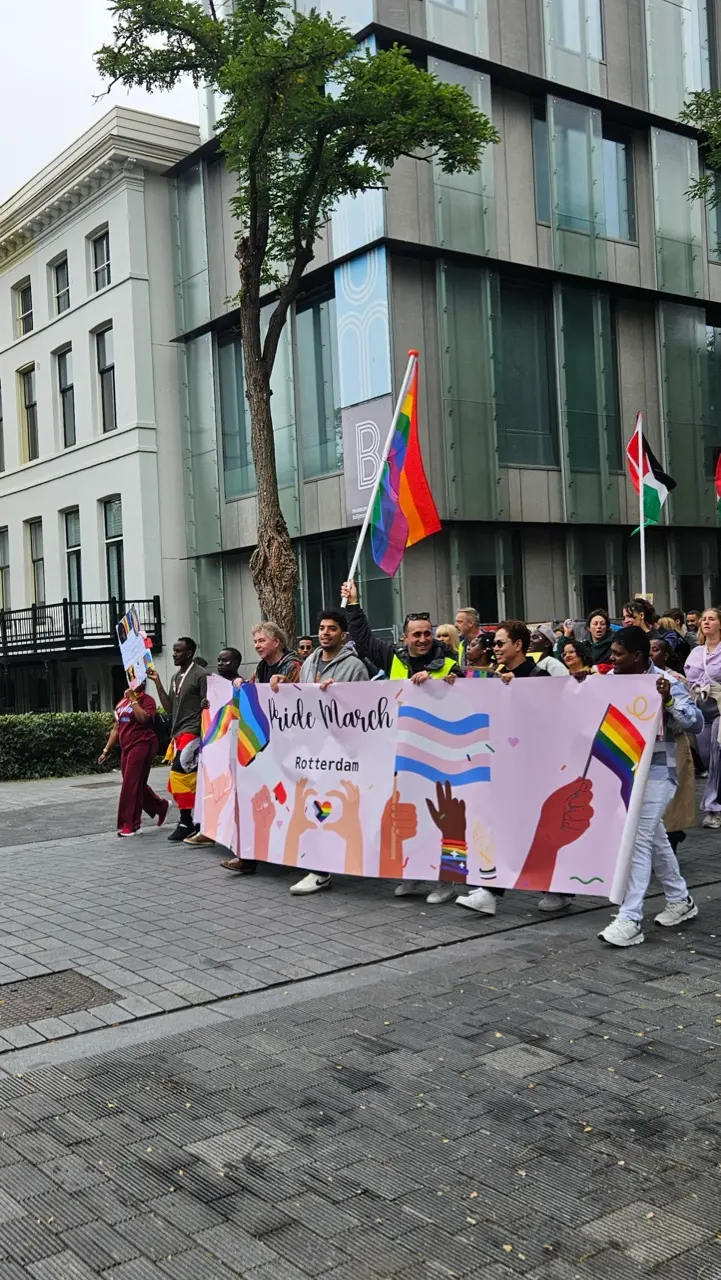 A crowd of people holding rainbow flags at a Pride event in Rotterdam.